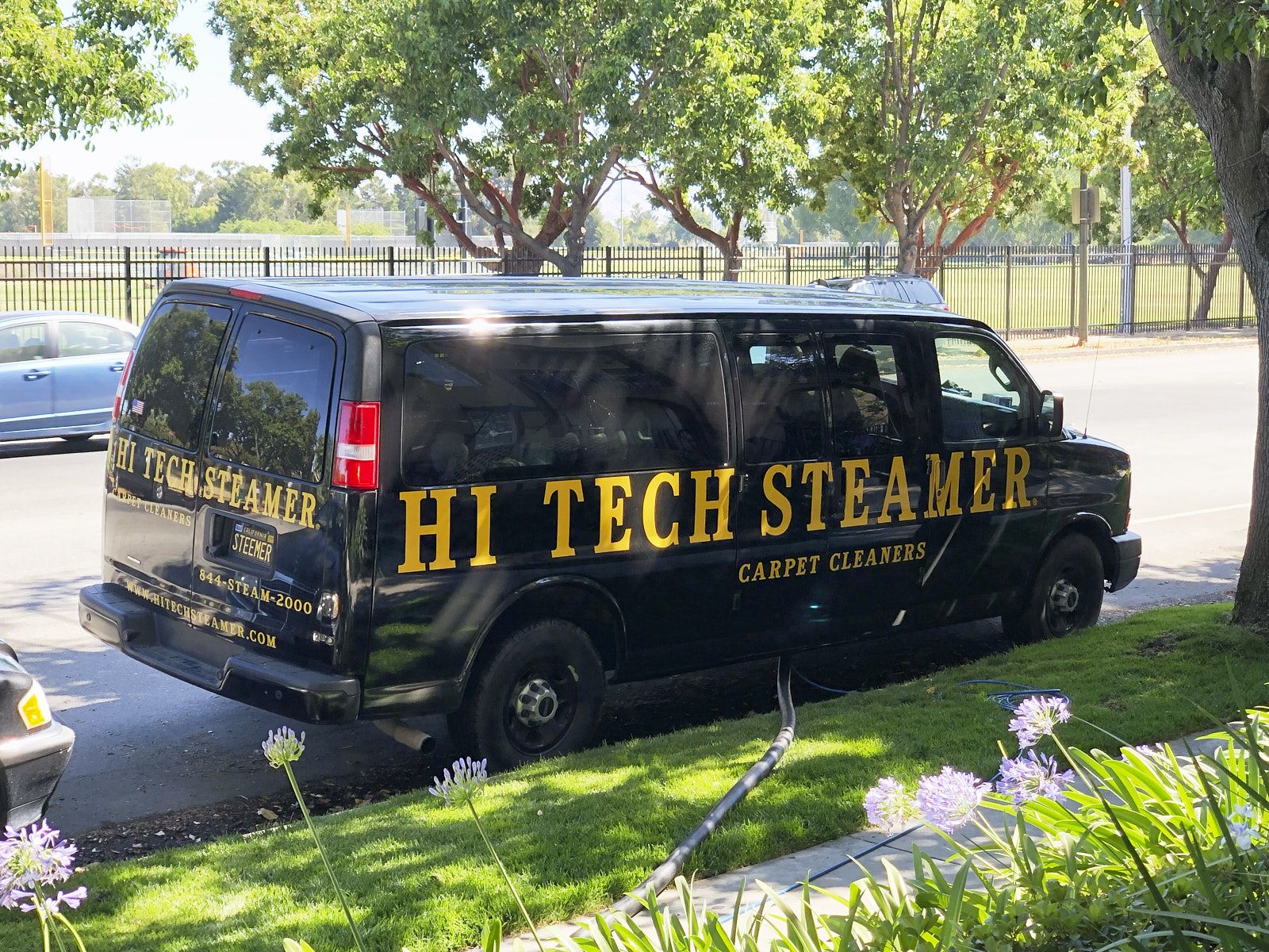 A Black Van From Hi Tech Steamer Is Parked In The Front Yard With A Water Pipeline Leading Towards The House