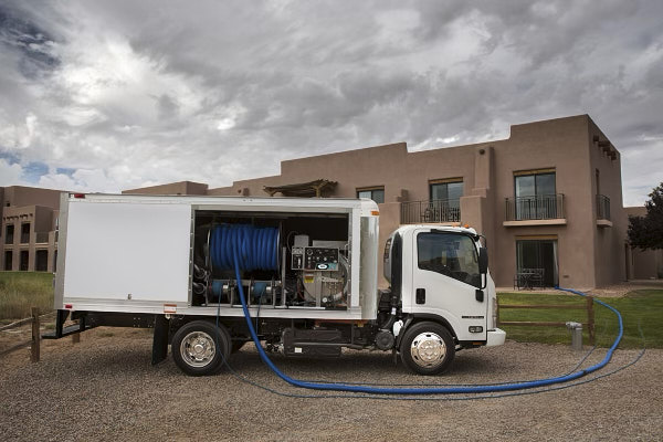 Side View Of A Large White Truck With A Water Line Leading Inside A House For The Carpet Cleaning Process.